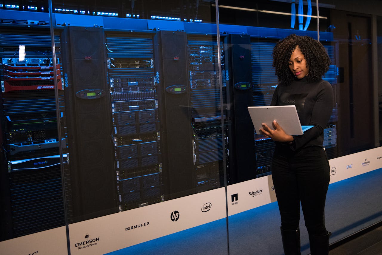 our-services-2 A female engineer using a laptop while monitoring data servers in a modern server room.